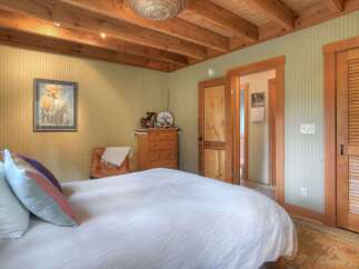 Experience rustic charm in this inviting bedroom, featuring exposed wooden beams on the ceiling and a cozy, light green paneled wall.