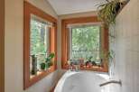 Bathe in nature's embrace with this stunning bathroom featuring a deep soaking tub positioned perfectly beneath two large windows.