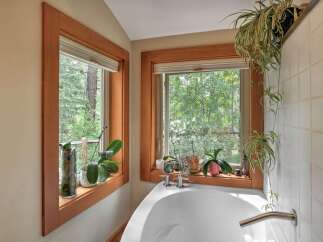 Bathe in nature's embrace with this stunning bathroom featuring a deep soaking tub positioned perfectly beneath two large windows.