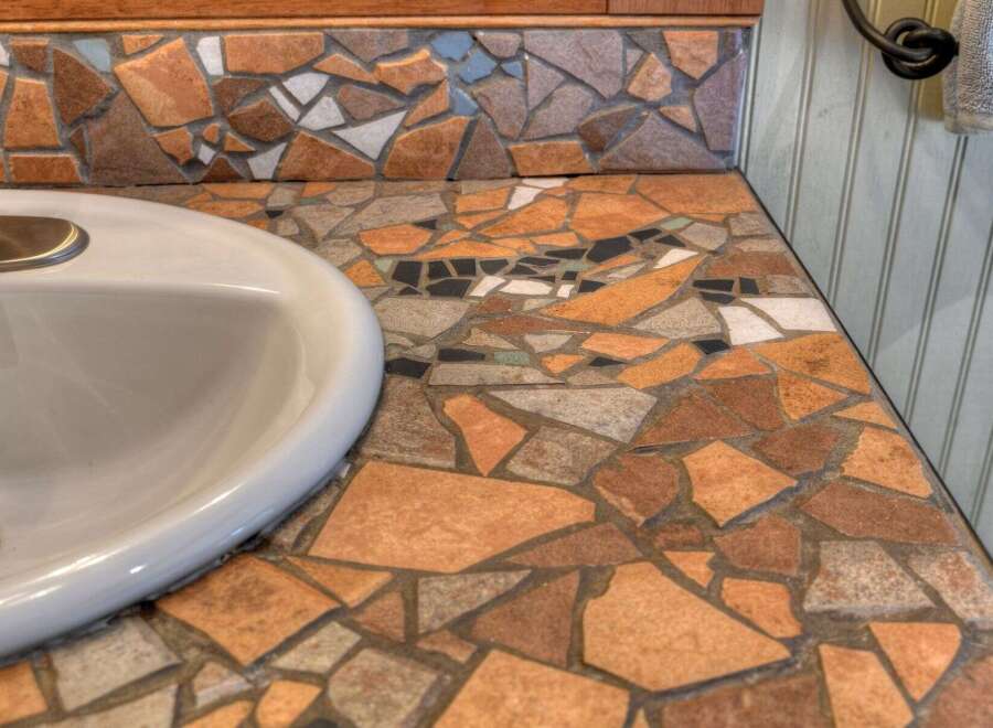 This bathroom vanity features a unique mosaic countertop with a variety of earth-toned tiles, creating a rustic and artistic focal point.