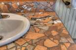 This bathroom vanity features a unique mosaic countertop with a variety of earth-toned tiles, creating a rustic and artistic focal point.