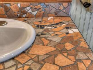This bathroom vanity features a unique mosaic countertop with a variety of earth-toned tiles, creating a rustic and artistic focal point.