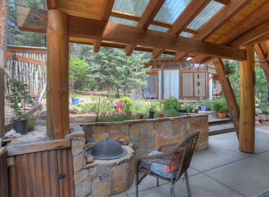 Enjoy outdoor living in this charming covered patio space, featuring a built-in stone grill and a rustic corrugated metal cabinet.