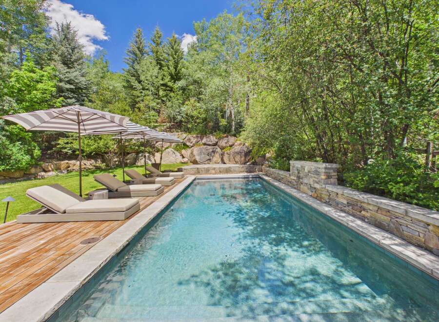 Escape to this serene backyard oasis featuring a sparkling swimming pool surrounded by lush greenery and mature trees.