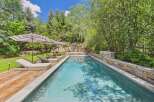 Escape to this serene backyard oasis featuring a sparkling swimming pool surrounded by lush greenery and mature trees.