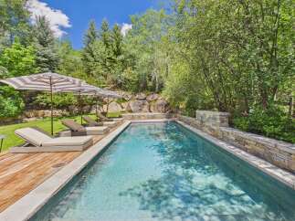 Escape to this serene backyard oasis featuring a sparkling swimming pool surrounded by lush greenery and mature trees.