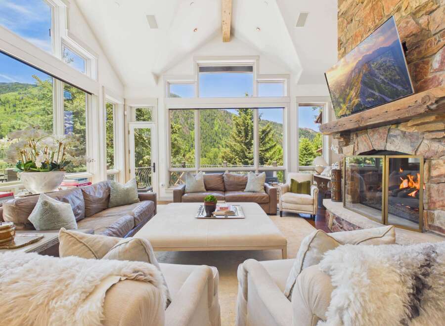 Experience luxury mountain living in this stunning great room, featuring a grand stone fireplace and expansive windows that frame breathtaking panoramic views.