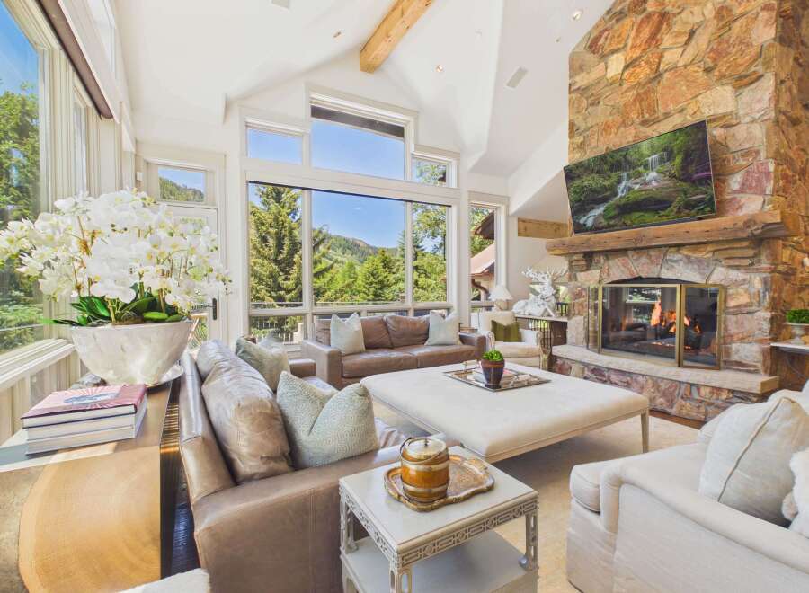 Experience breathtaking mountain views from this stunning living room, featuring a grand stone fireplace and expansive windows.
