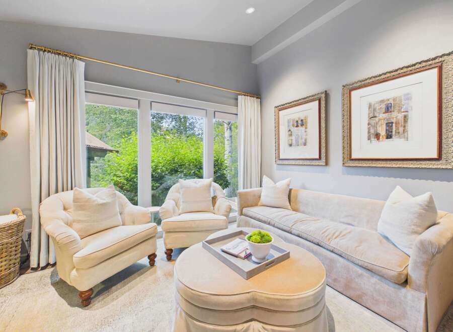 Step into this inviting living room, bathed in natural light from expansive windows overlooking lush greenery.