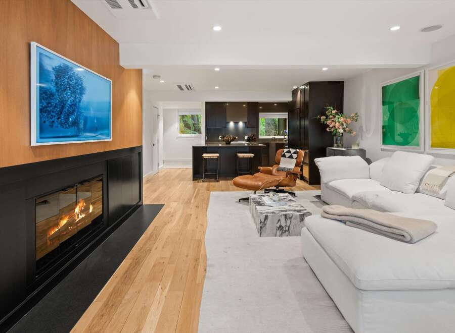 Experience modern living in this stunning open-concept space, featuring a sleek fireplace with a captivating artwork above and a gourmet kitchen with dark cabinetry and bar seating.