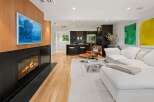 Experience modern living in this stunning open-concept space, featuring a sleek fireplace with a captivating artwork above and a gourmet kitchen with dark cabinetry and bar seating.
