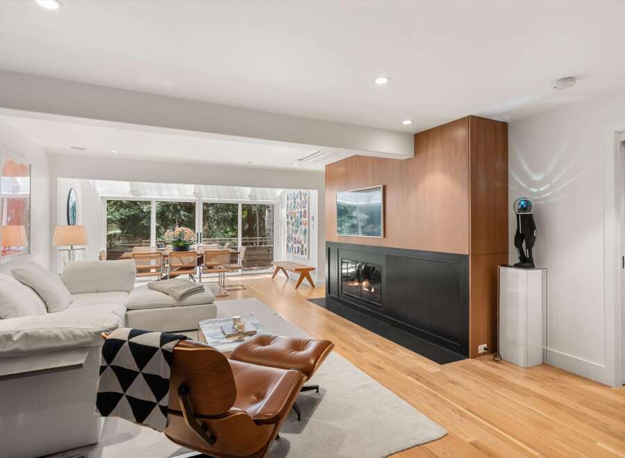 Experience modern living in this stunning open-concept living space, featuring a sleek fireplace with a warm wood accent wall and a mounted television.