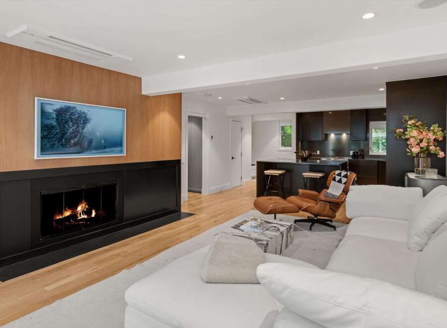 Experience modern living in this stunning open-concept space, featuring a sleek fireplace with a wood-paneled accent wall and a large flat-screen TV.
