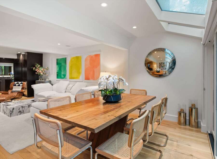 Experience modern living in this stunning open-concept space, featuring a sleek dining area with a natural wood table and cane-backed chairs, complemented by vibrant abstract art.
