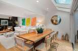 Experience modern living in this stunning open-concept space, featuring a sleek dining area with a natural wood table and cane-backed chairs, complemented by vibrant abstract art.