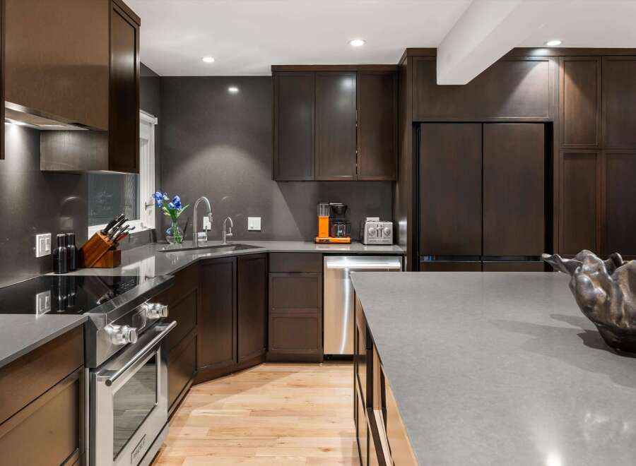 Experience luxury in this modern kitchen featuring dark wood cabinetry and sleek gray countertops.