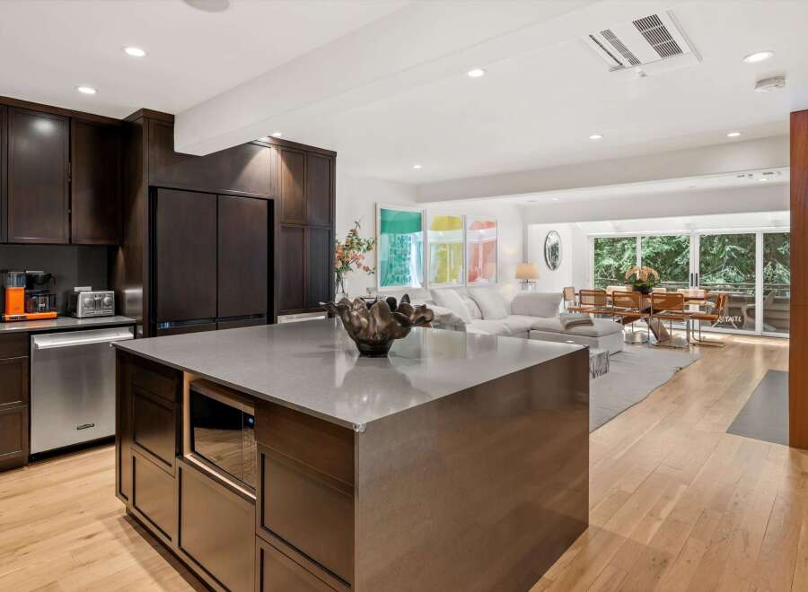 Experience modern living in this open-concept kitchen and living area, featuring dark wood cabinetry, a sleek gray island with a built-in microwave, and stainless steel appliances.