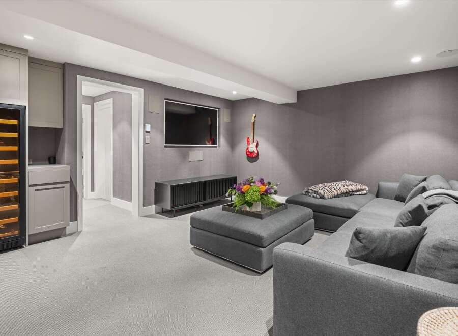 This modern living space features a sleek entertainment center with a wall-mounted TV, complemented by a comfortable sectional sofa and a stylish ottoman adorned with a floral arrangement.