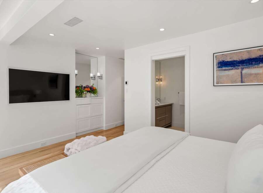 Experience modern luxury in this stunning bedroom featuring a wall-mounted TV and a plush white throw.