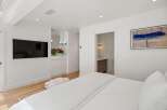 Experience modern luxury in this stunning bedroom featuring a wall-mounted TV and a plush white throw.