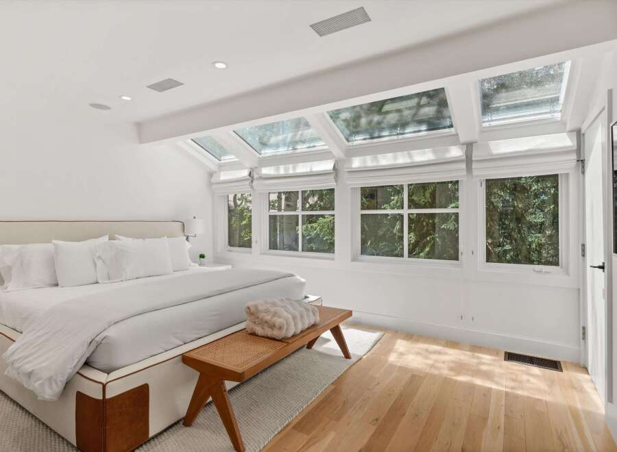 Experience natural light like never before in this stunning bedroom, featuring expansive skylights and large windows that offer serene views of lush greenery.