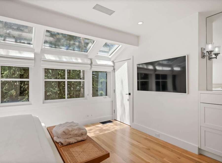 Experience natural light and serene views from this bedroom, featuring expansive skylights and large windows overlooking lush greenery.