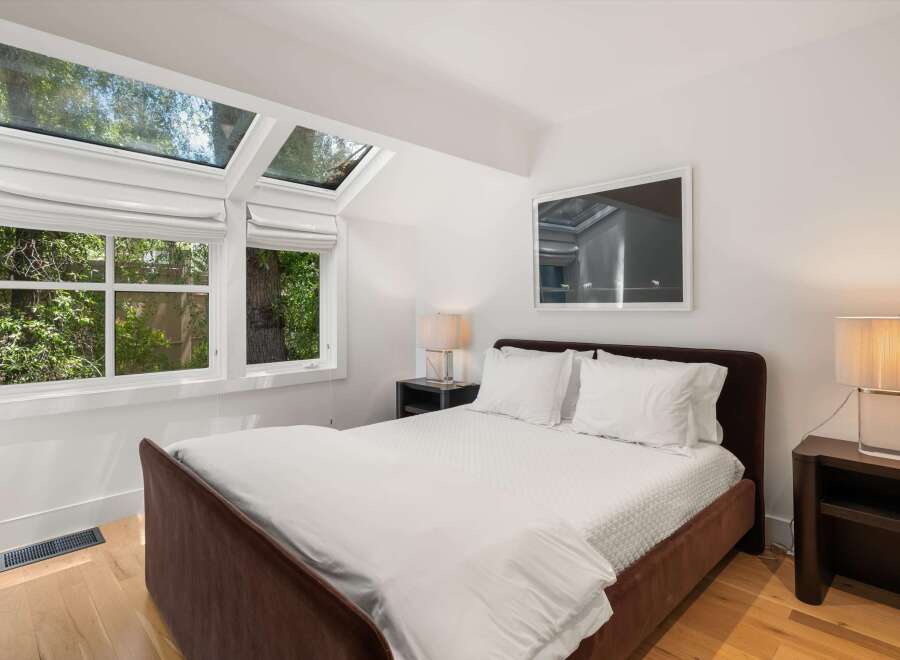 Experience natural light and serene views in this inviting bedroom, featuring expansive skylights and large windows that overlook lush greenery.