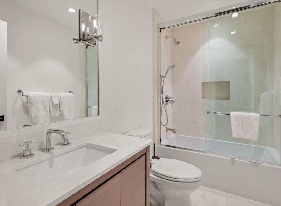 Experience modern luxury in this stunning bathroom featuring a sleek vanity with a marble countertop and a spacious bathtub/shower combination enclosed by a glass door.