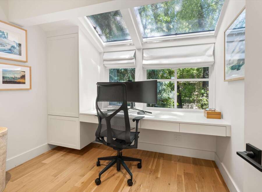 This home office features a sleek white built-in desk with ample storage, complemented by a modern black mesh office chair.