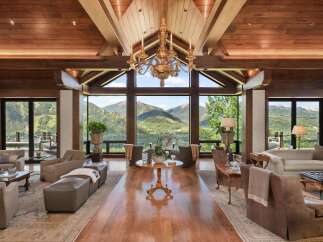 Experience luxury mountain living in this stunning great room, featuring a soaring wood-beamed ceiling and a magnificent gold chandelier.