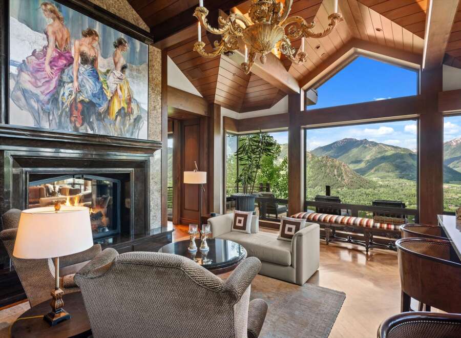 Experience breathtaking mountain views from this luxurious living room, featuring a grand fireplace and a stunning chandelier.