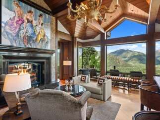 Experience breathtaking mountain views from this luxurious living room, featuring a grand fireplace and a stunning chandelier.