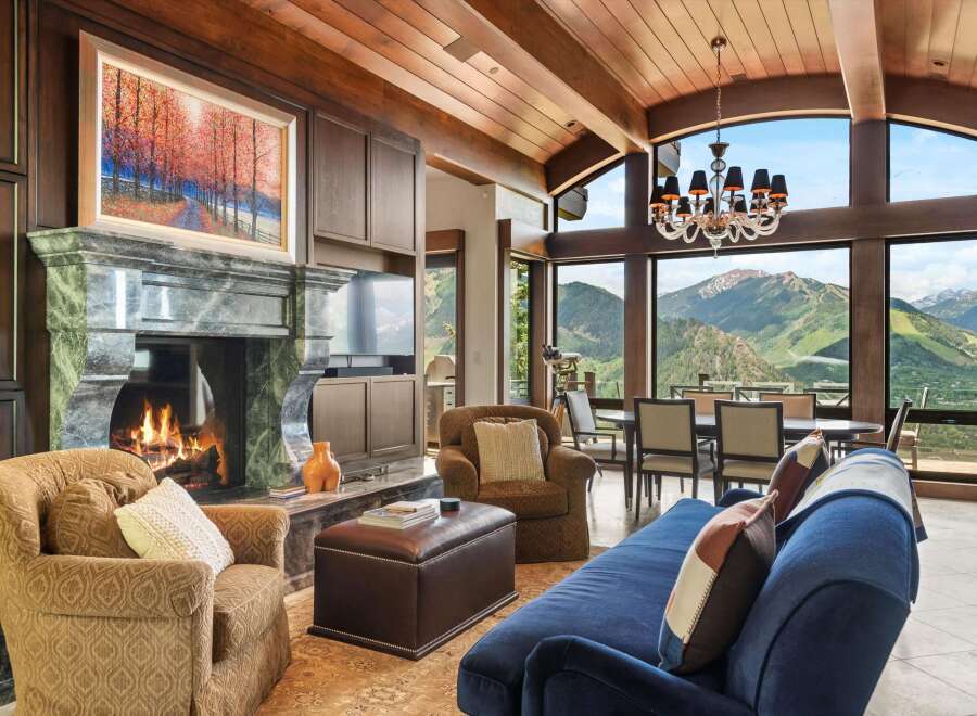 Experience breathtaking mountain views from this luxurious living room, featuring a grand marble fireplace and a stunning chandelier.