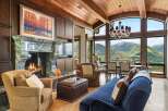 Experience breathtaking mountain views from this luxurious living room, featuring a grand marble fireplace and a stunning chandelier.