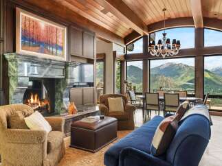 Experience breathtaking mountain views from this luxurious living room, featuring a grand marble fireplace and a stunning chandelier.