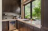 This kitchen area features dark wood cabinetry and a granite countertop, complemented by a stainless steel sink and a built-in beverage cooler.