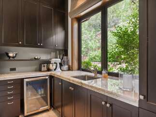 This kitchen area features dark wood cabinetry and a granite countertop, complemented by a stainless steel sink and a built-in beverage cooler.
