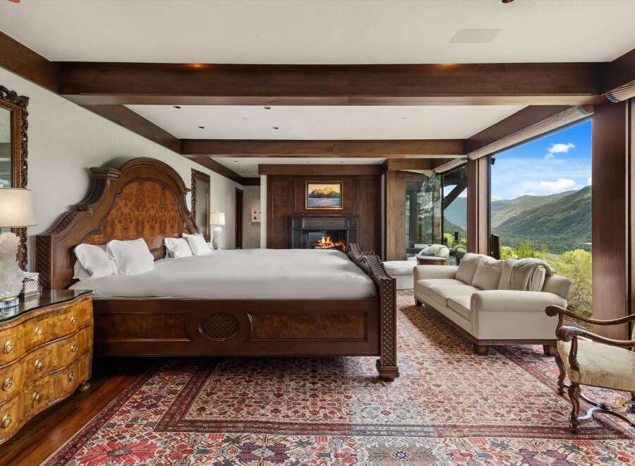 Experience luxury mountain living in this exquisite bedroom featuring a grand wooden bed and a cozy fireplace.