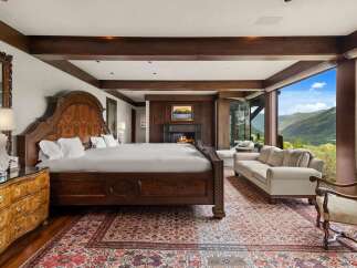 Experience luxury mountain living in this exquisite bedroom featuring a grand wooden bed and a cozy fireplace.
