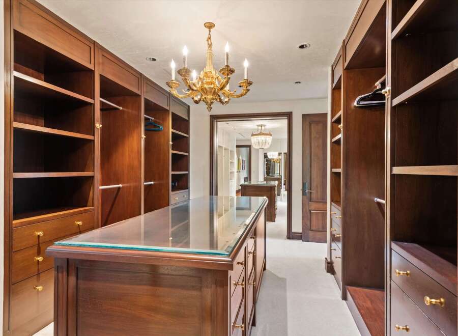 Step into this luxurious walk-in closet, featuring rich mahogany built-ins and a central island with a glass top.