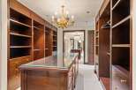 Step into this luxurious walk-in closet, featuring rich mahogany built-ins and a central island with a glass top.