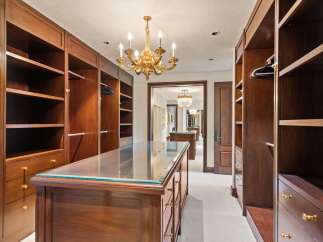 Step into this luxurious walk-in closet, featuring rich mahogany built-ins and a central island with a glass top.