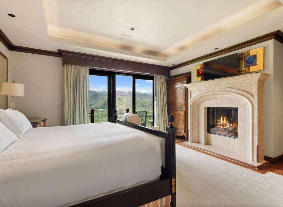 Experience luxury mountain living in this exquisite bedroom, featuring a cozy fireplace and breathtaking panoramic views of the surrounding peaks.
