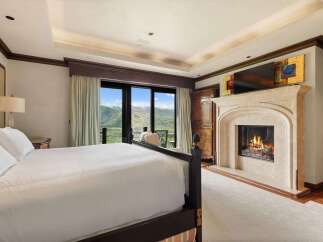Experience luxury mountain living in this exquisite bedroom, featuring a cozy fireplace and breathtaking panoramic views of the surrounding peaks.