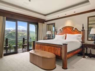Experience luxury mountain living in this stunning bedroom featuring a grand wooden bed and a plush leather ottoman.