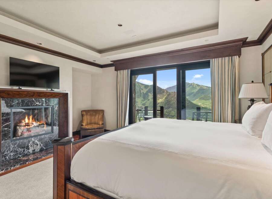 Experience luxury mountain living in this stunning bedroom featuring a cozy fireplace with marble surround and a large flat-screen TV.