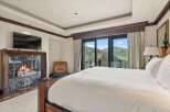 Experience luxury mountain living in this stunning bedroom featuring a cozy fireplace with marble surround and a large flat-screen TV.