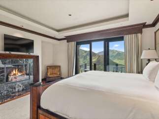 Experience luxury mountain living in this stunning bedroom featuring a cozy fireplace with marble surround and a large flat-screen TV.