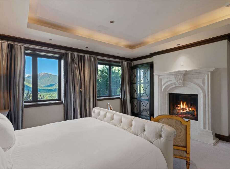 Experience luxury mountain living in this exquisite bedroom, featuring a plush tufted bed and a grand stone fireplace perfect for cozy evenings.