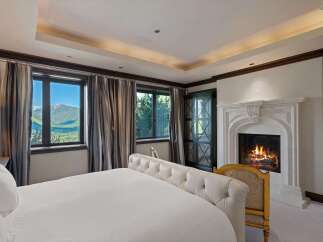 Experience luxury mountain living in this exquisite bedroom, featuring a plush tufted bed and a grand stone fireplace perfect for cozy evenings.